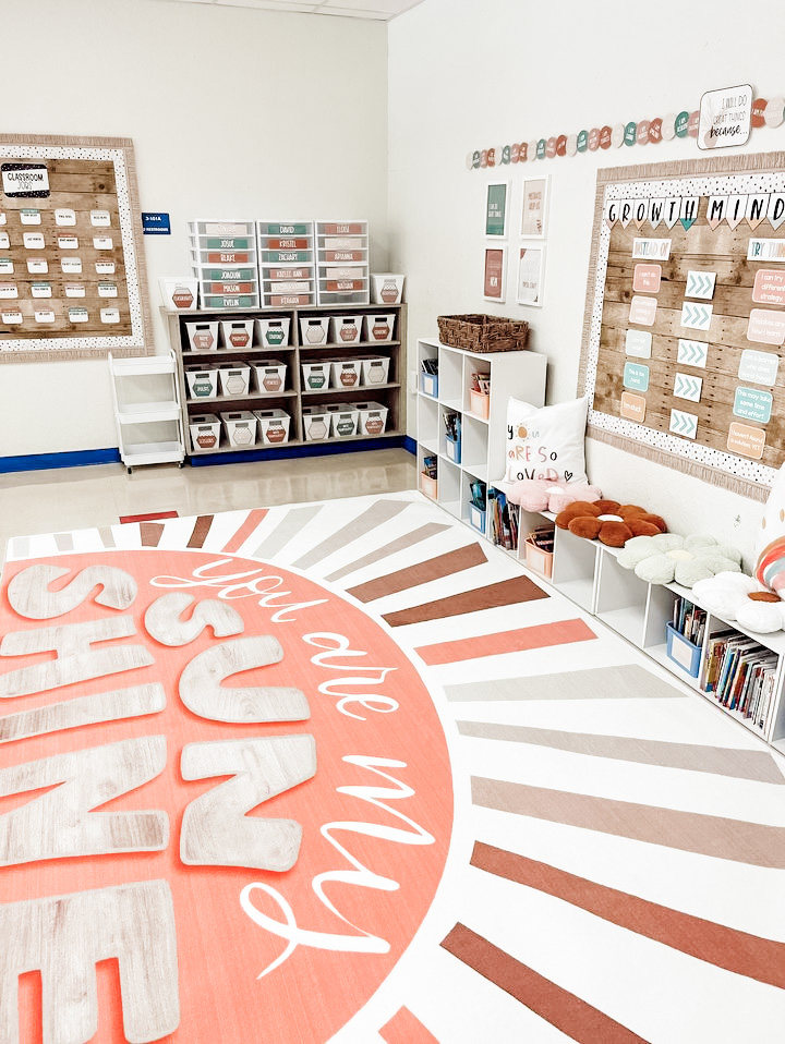 This image shows a classroom decorated with the simply neutral decor. There is a fun rug that says You are my Sunshine on the floor, lots of bookcases, and other cubes for storage.