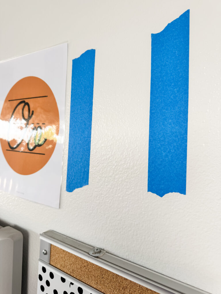 This image shows a close-up of blue painter's tape on the wall where a poster will be hung.
