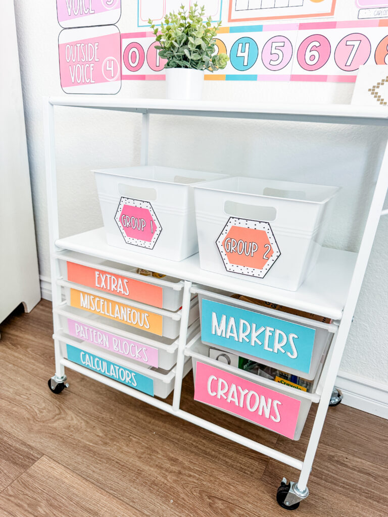 This image shows a rolling cart with white buckets on top for storage. The drawers and the buckets all have bright, editable labels indicating what item is stored inside.