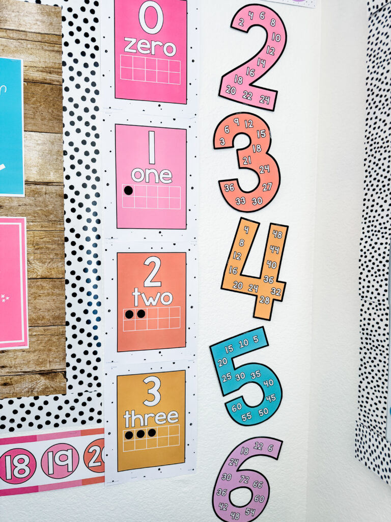 This image shows number posters and skip counting posters next to a bulletin board on the side of a classroom wall.