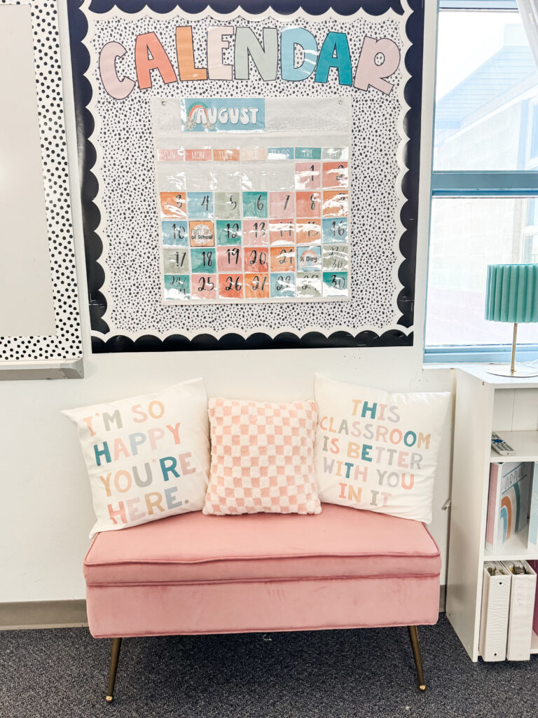 This image shows a bulletin board with a calendar pocket chart above a small, cute, pink couch.