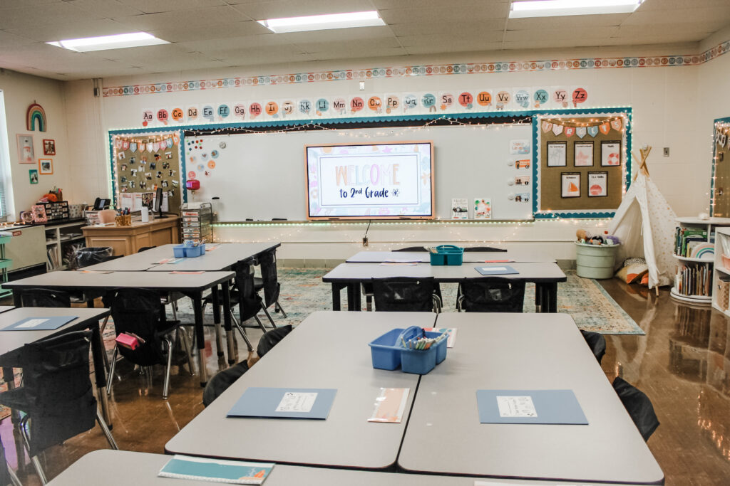 This image shows a 2nd grade classroom with tables in groups and lots of cute, decor ideas. 