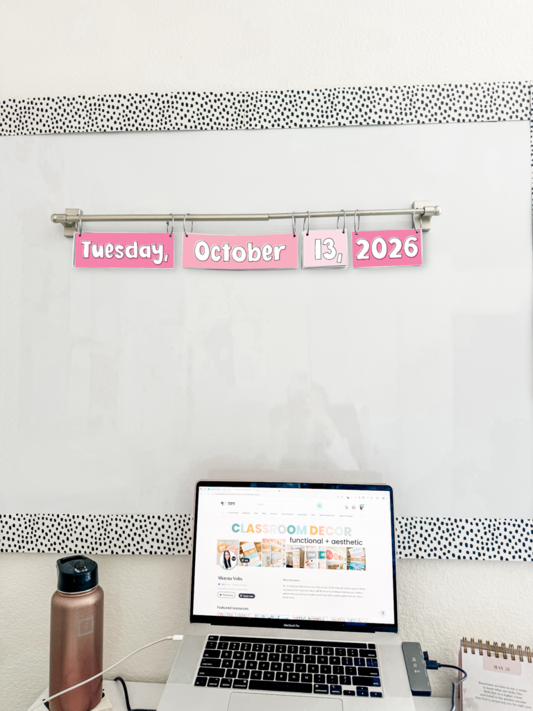 This image shows a pink flip calendar hanging on a magnetic rod on a whiteboard. 
