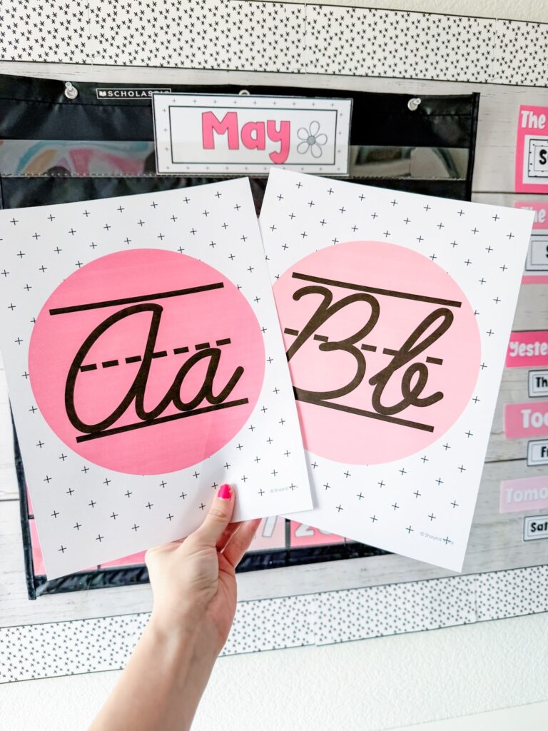 This image shows two cursive alphabet posters included in this classroom decor bundle. Each poster has the upper and lowercase letter in a pink circle in the middle of the poster. The rest of the poster is white with small, black plus signs as the background. 