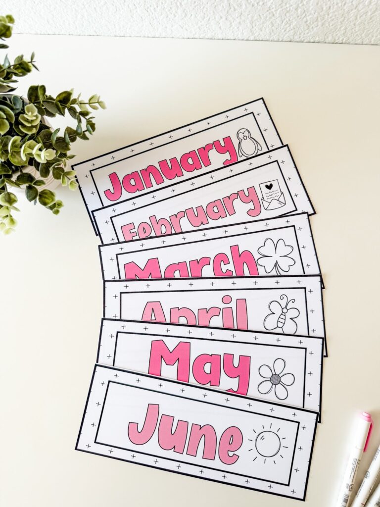 This image shows a close-up of month cards. Each month card has the text in a shade of pink bubble letters. Next to the name of the month is a sketch drawing of some little icon that is connected to the month of the year. 