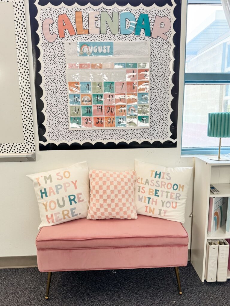 This image shows a calendar display above a cute, pink couch with three pillows sitting on top of it.