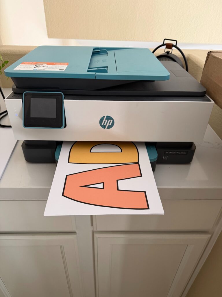 This image shows a home printer spitting out bulletin board letters from a printable classroom decor bundle.
