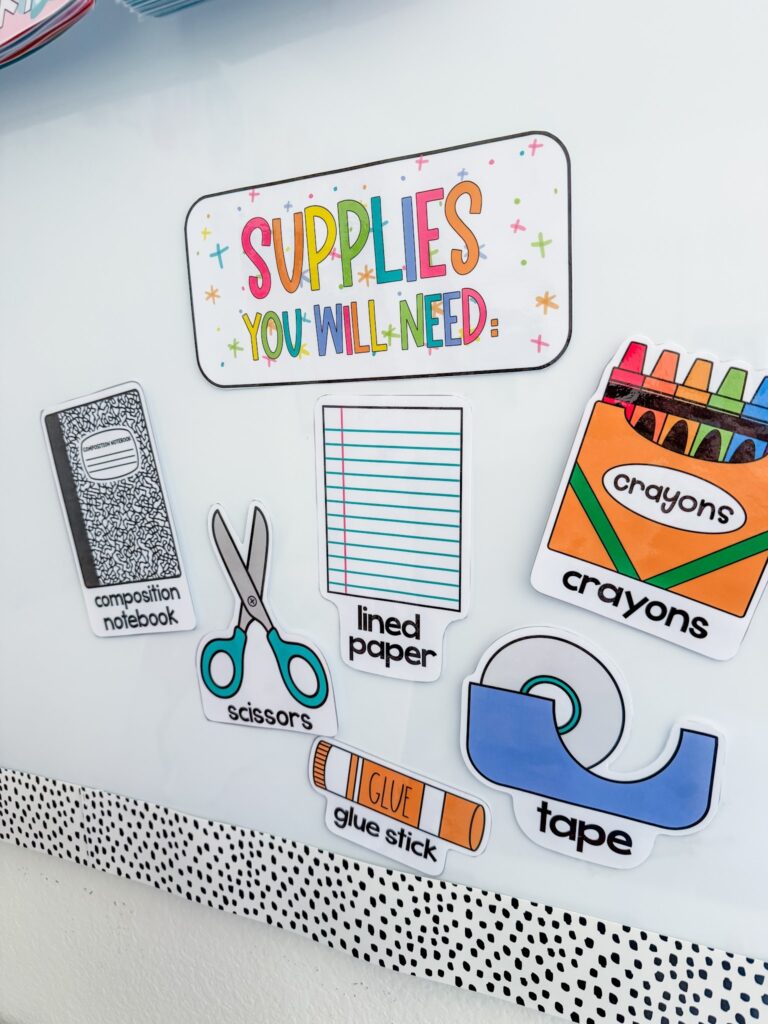 This image shows the supplies you will need display on a whiteboard decorated in the happy hues design. There is a poster at the top that reads, "Supplies You Will Need" and then you can see clipart images with labels: composition notebook, scissors, lined paper, crayons, glue stick, and tape. 