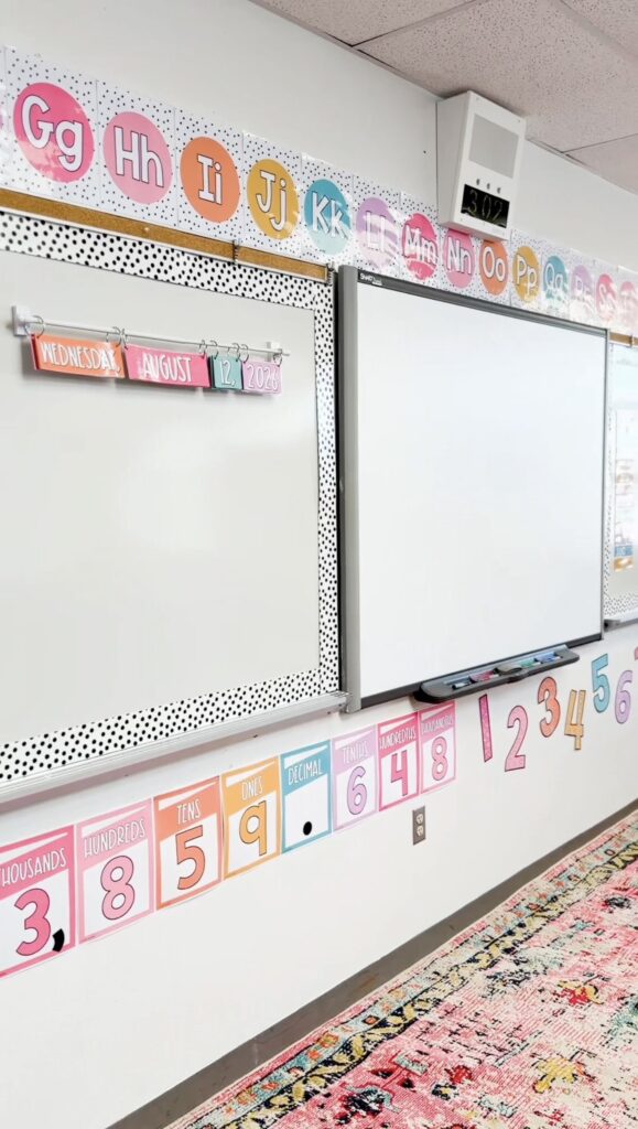 This image shows a close-up of the front of the classroom whiteboard with alphabet posters running along the top of the board. Along the bottom of the board are place value posters and skip counting numbers.