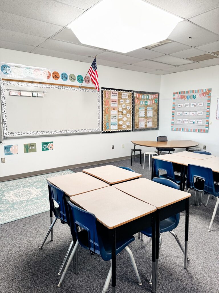 This image shows student desks in groups of four, a small group table in the corner, and decorations on the walls of this clasroom.