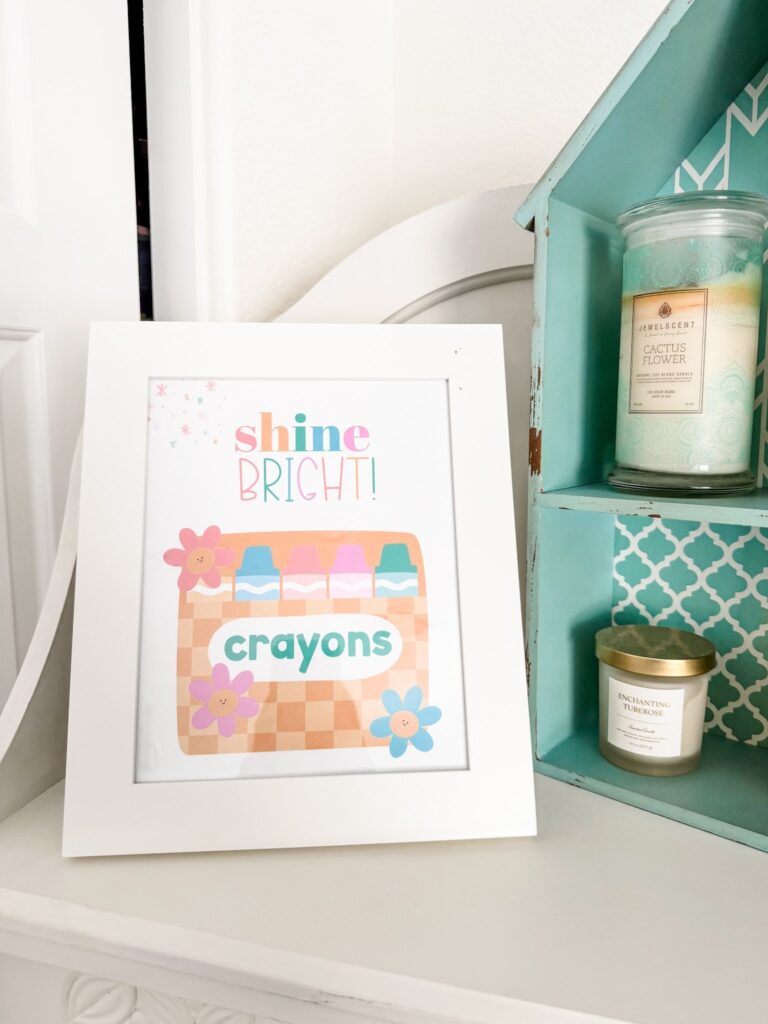 This image shows an inspirational poster in a white frame. The poster says "Shine Bright" and has a picture of crayons at the bottom.