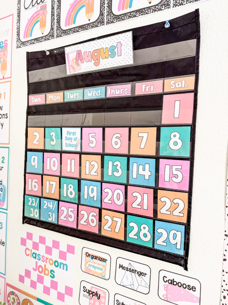This image shows a pastel classroom calendar in a black pocket chart.