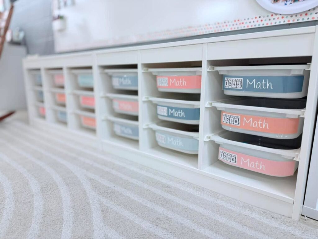 This image shows a close-up of the storage bins underneath the main whiteboard in the PK classroom. Each bucket has either a Math or Literacy label. 