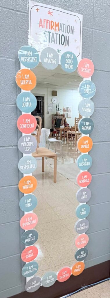This image shows an affirmation mirror in this Pre-K classroom. There is a white mirror with Modern Calm Color circles surrounding the mirror with "I am" statements. 