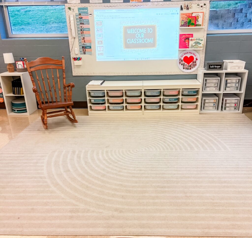 This image shows the front whiteboard area in a pk classroom. The area is spacious, has a large rug on the floor, and a rocking chair off to the side of the whiteboard. 