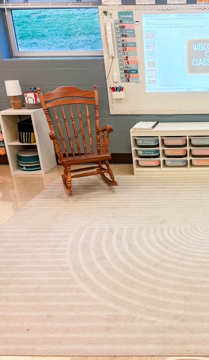 This image shows the front whiteboard area in a pk classroom. The area is spacious, has a large rug on the floor, and a rocking chair off to the side of the whiteboard.
