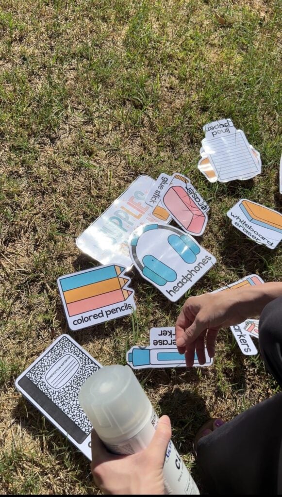 This image shows a teacher spreading decor display pieces that are laminated out on the grass. You can see a glare from where the sun hits the laminated items.